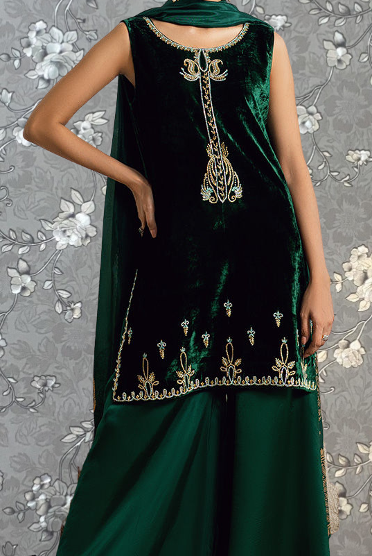 A woman wearing a green velvet dress with gold embroidery and a matching green skirt.