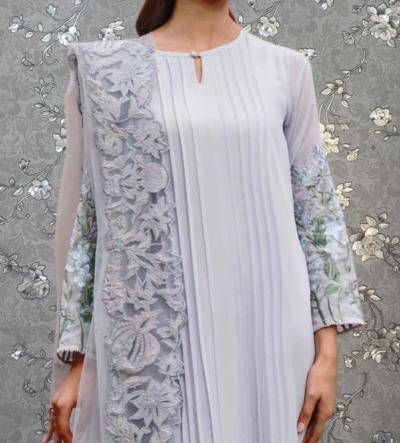A woman wearing a long, white dress with intricate floral embroidery on the sleeves and a pleated neckline.
