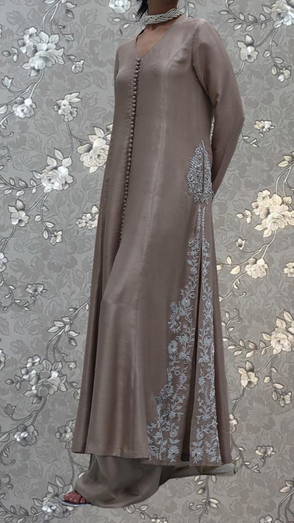 A woman wearing a long, beige dress with intricate embroidered patterns on the side.