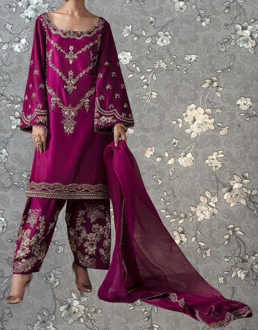 A woman wearing a vibrant purple dress with intricate embroidery and floral patterns, standing against a gray floral background.