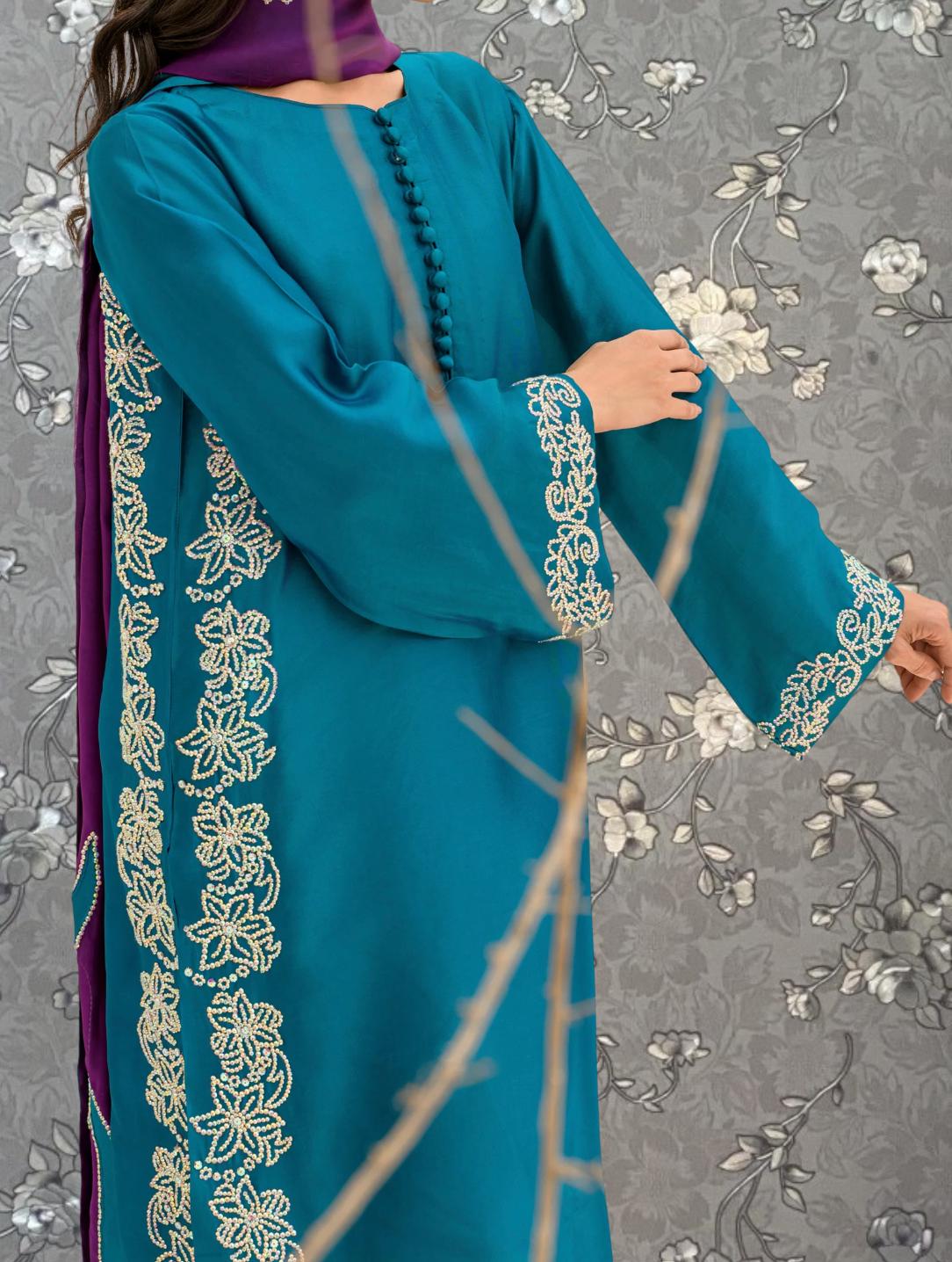 A person wearing a teal blue dress with intricate embroidered patterns on the sleeves and hem.