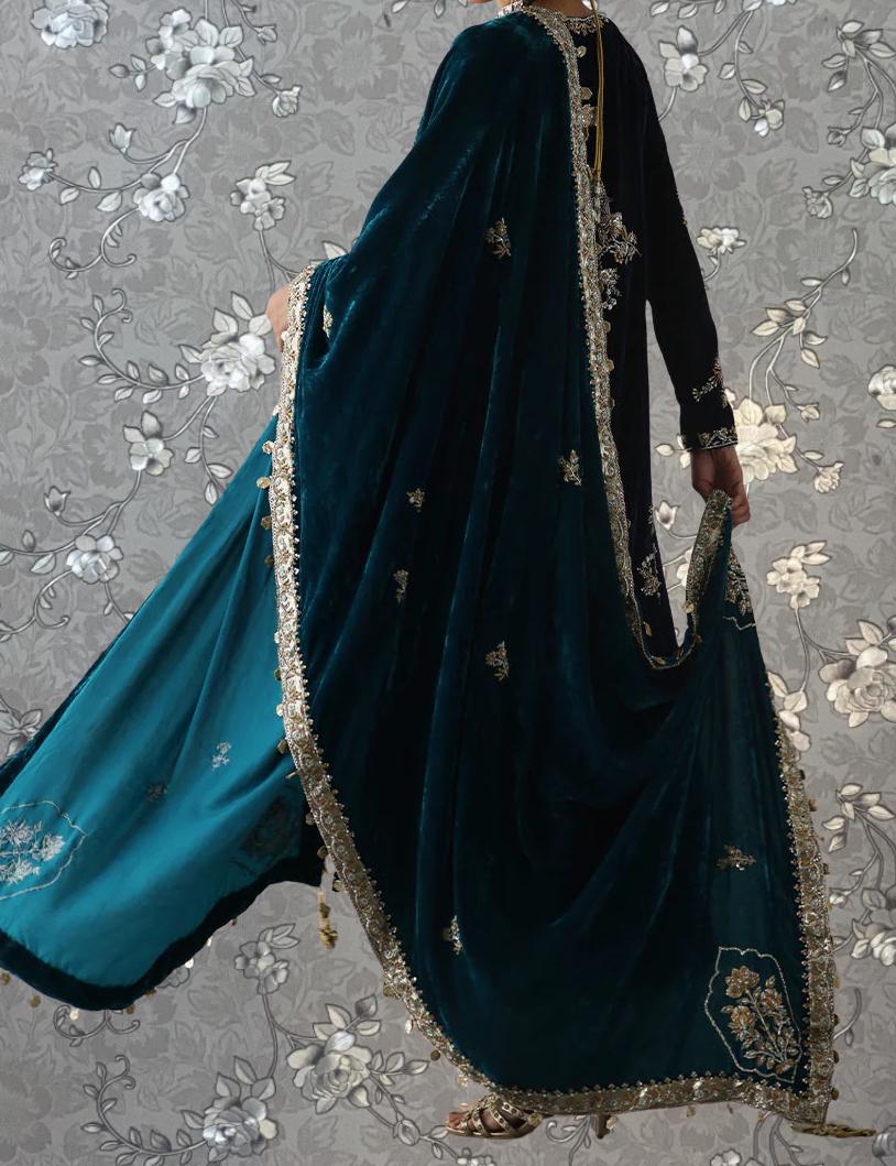 A person wearing a long, dark green velvet shawl with gold embroidery and a matching green velvet skirt.