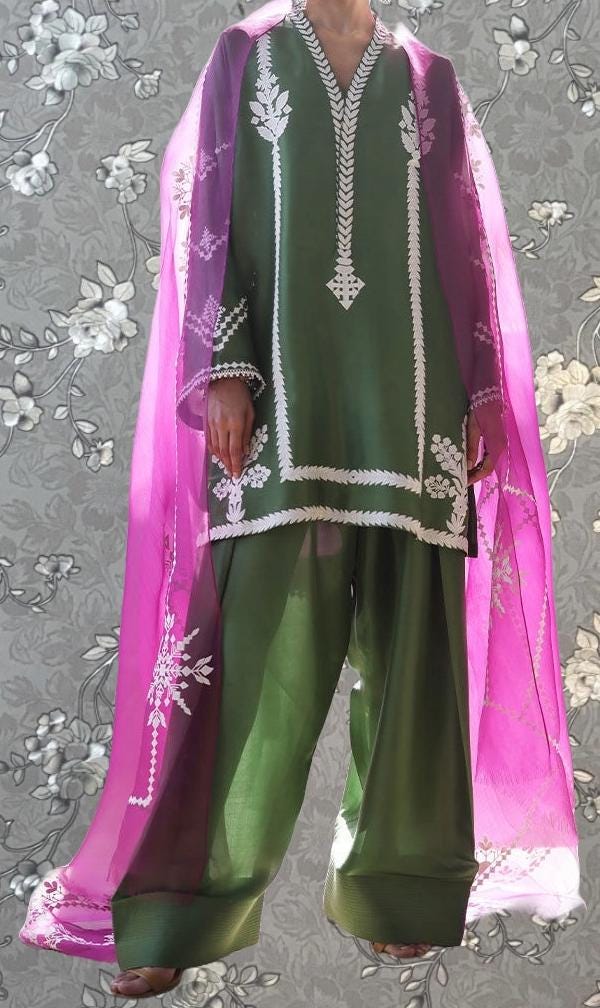 A person wearing a green and pink patterned outfit with a pink shawl draped over their shoulders.