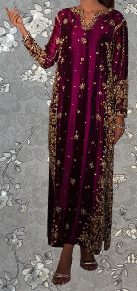 A woman wearing a long, burgundy dress with gold embroidery and a high neckline.