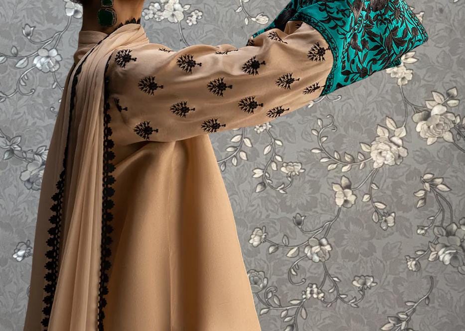 A person wearing a beige dress with black floral embroidery on the sleeves and a matching beige scarf.