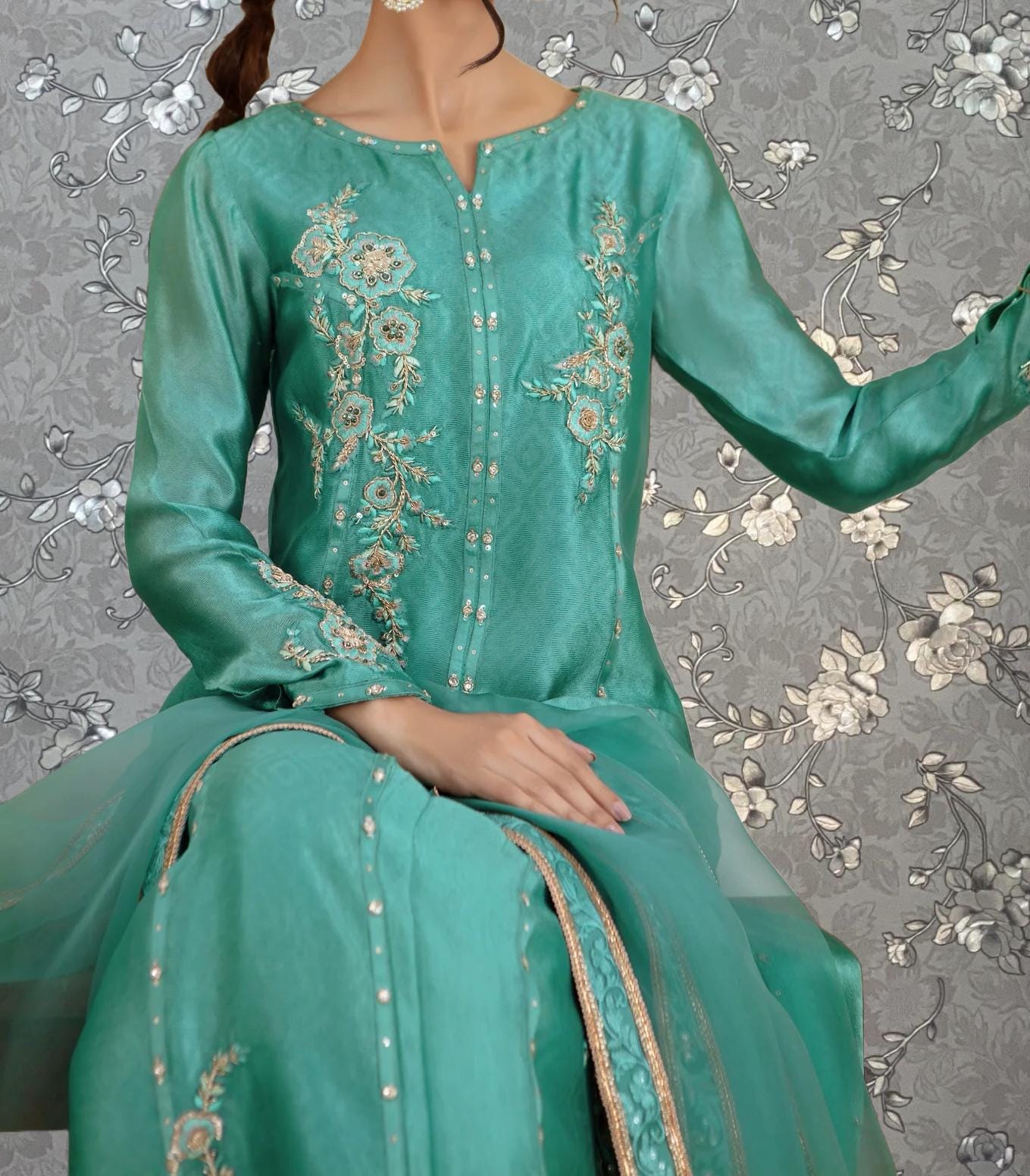 A woman wearing a turquoise dress with intricate floral embroidery on the front.