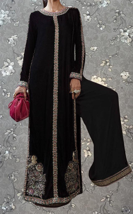 A woman wearing a long black dress with gold embroidery and a red purse is standing against a floral background.