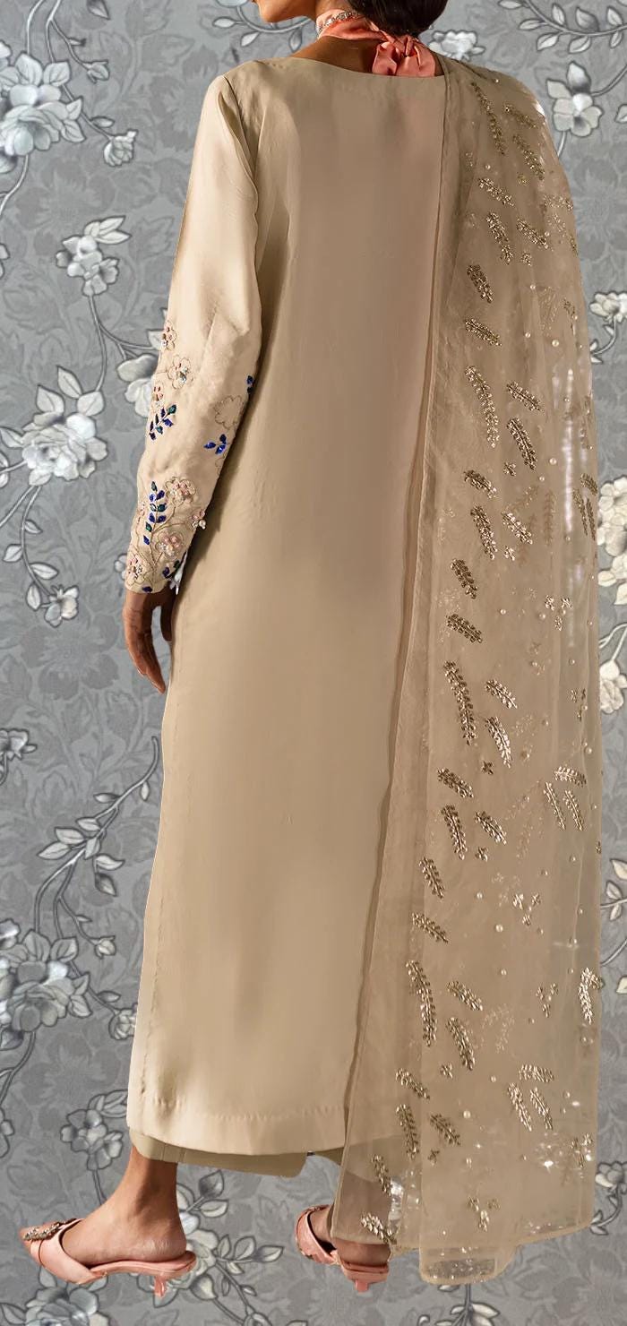 A person wearing a long, beige dress with intricate embroidery on the sleeves and a matching beige shawl with gold leaf embellishments.