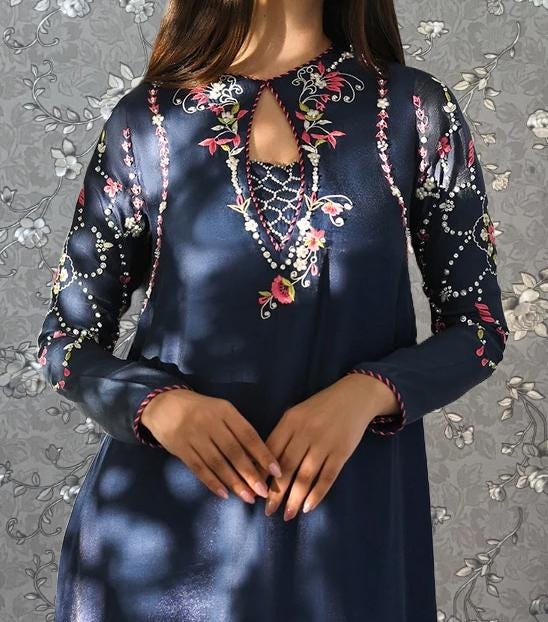 A woman wearing a blue dress with intricate floral embroidery on the sleeves and neckline.