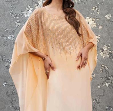 A woman wearing a peach-colored dress with a beaded pattern and a flowing, draped design.