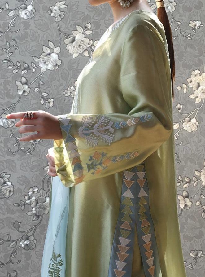 A woman wearing a green dress with intricate embroidered patterns on the sleeves and a floral pattern on the background.