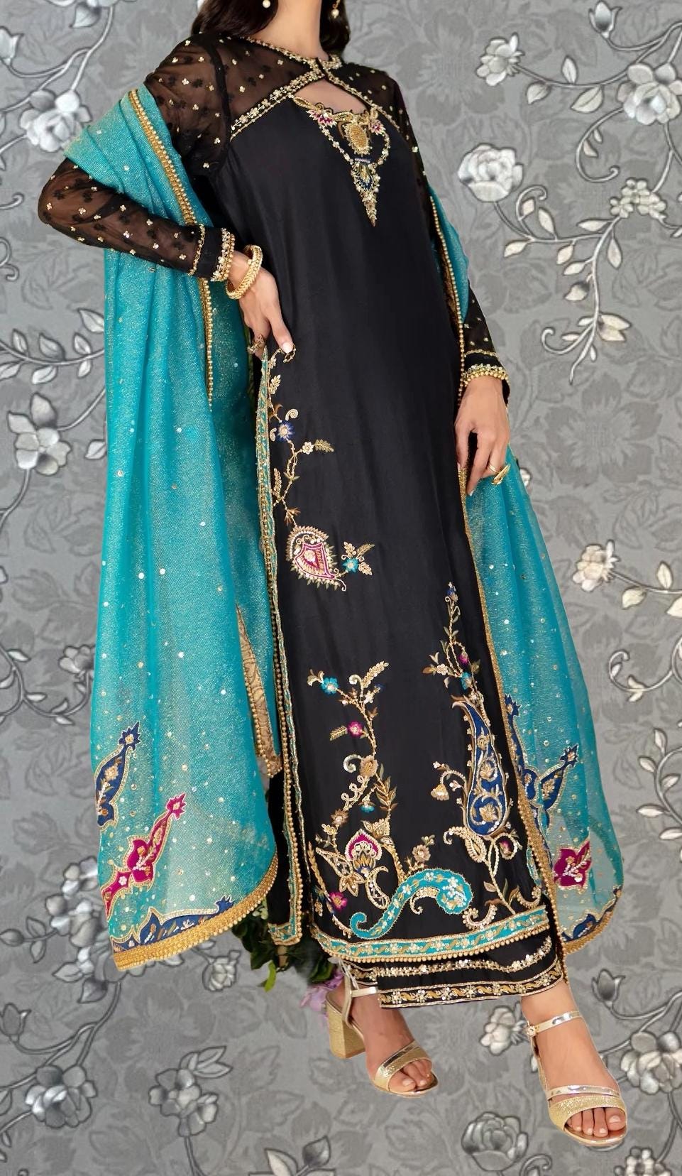 A woman wearing a long black dress with intricate gold embroidery and a turquoise shawl.