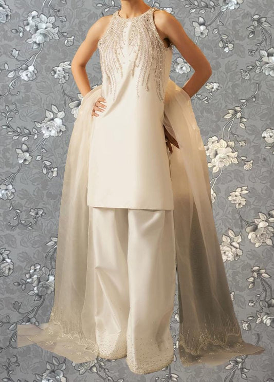A woman wearing a white dress with a beaded bodice and a long, flowing skirt stands against a gray floral background.