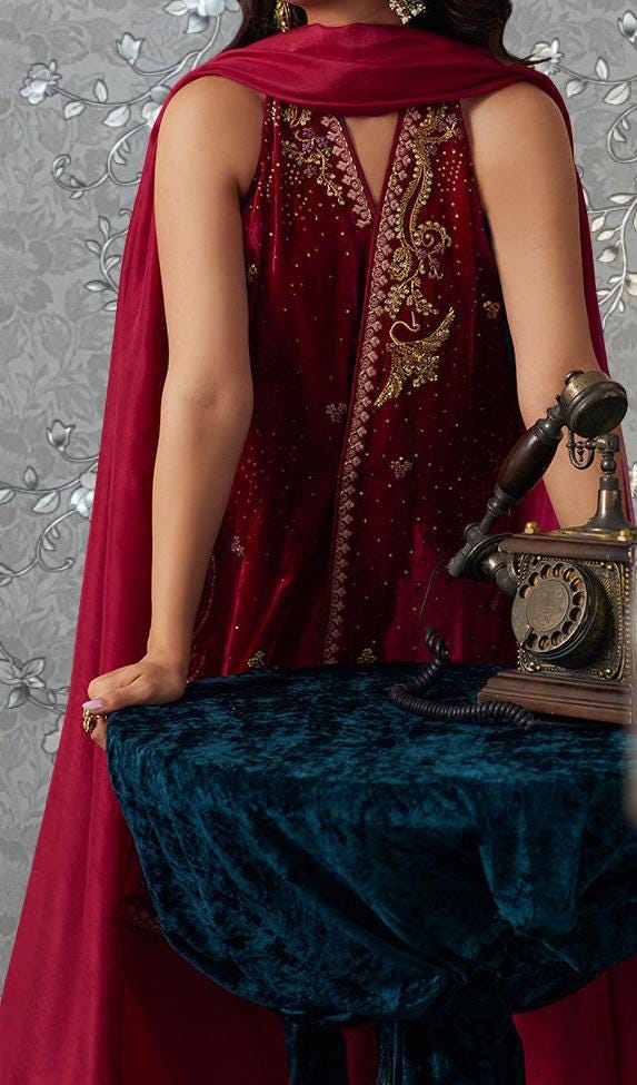 A woman wearing a red and gold dress stands in front of a floral patterned background, holding a vintage-style telephone.