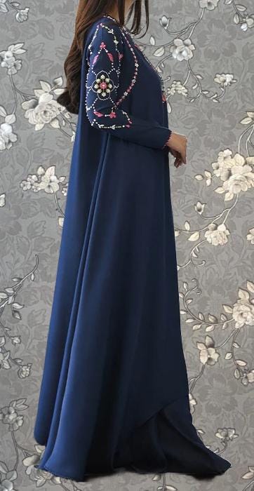 A woman wearing a long, navy blue dress with intricate embroidered designs on the sleeves and hem.