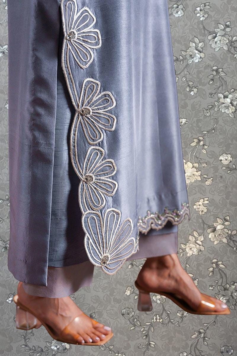 A close-up of a person's legs wearing a gray dress with intricate floral embroidery, paired with brown high-heeled shoes.