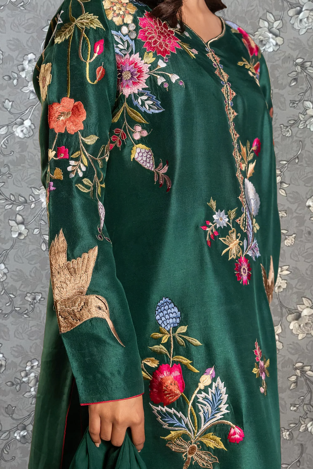 A close-up of a person wearing a green dress with intricate floral embroidery.