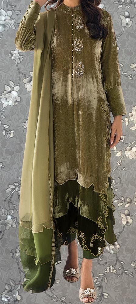 A woman wearing a green and gold dress with a long green shawl draped over her shoulders, standing against a gray floral background.