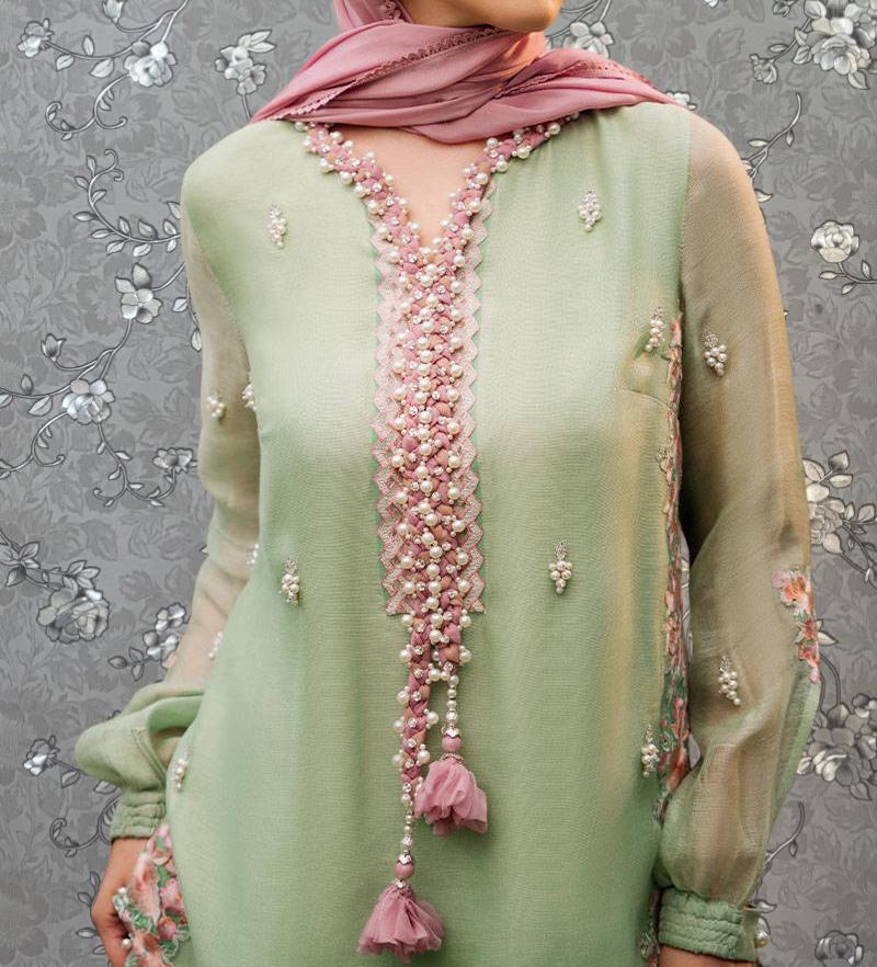 A woman wearing a green dress with pink and white embellishments, including a long beaded neckline and a long tassel.