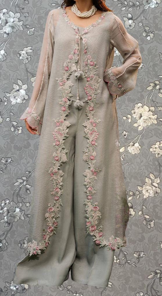 A woman wearing a long, light-colored dress with intricate floral embroidery on the sleeves and hem.