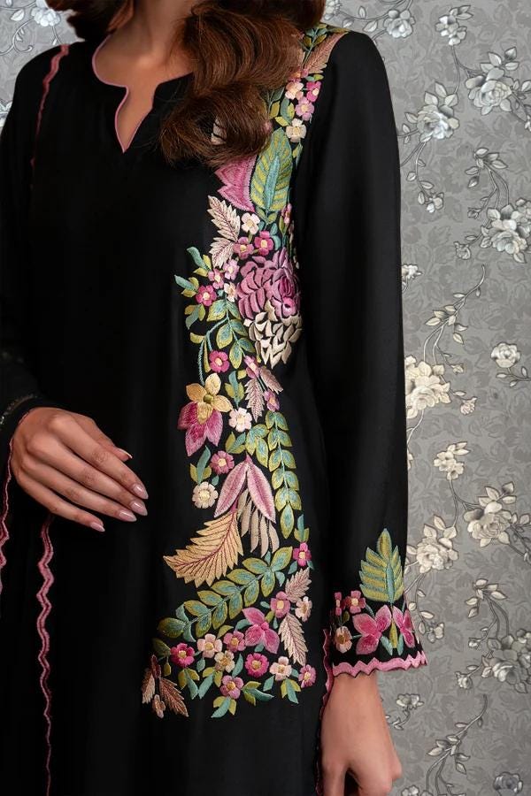 A close-up of a woman wearing a black dress with colorful floral embroidery on the sleeves and collar.