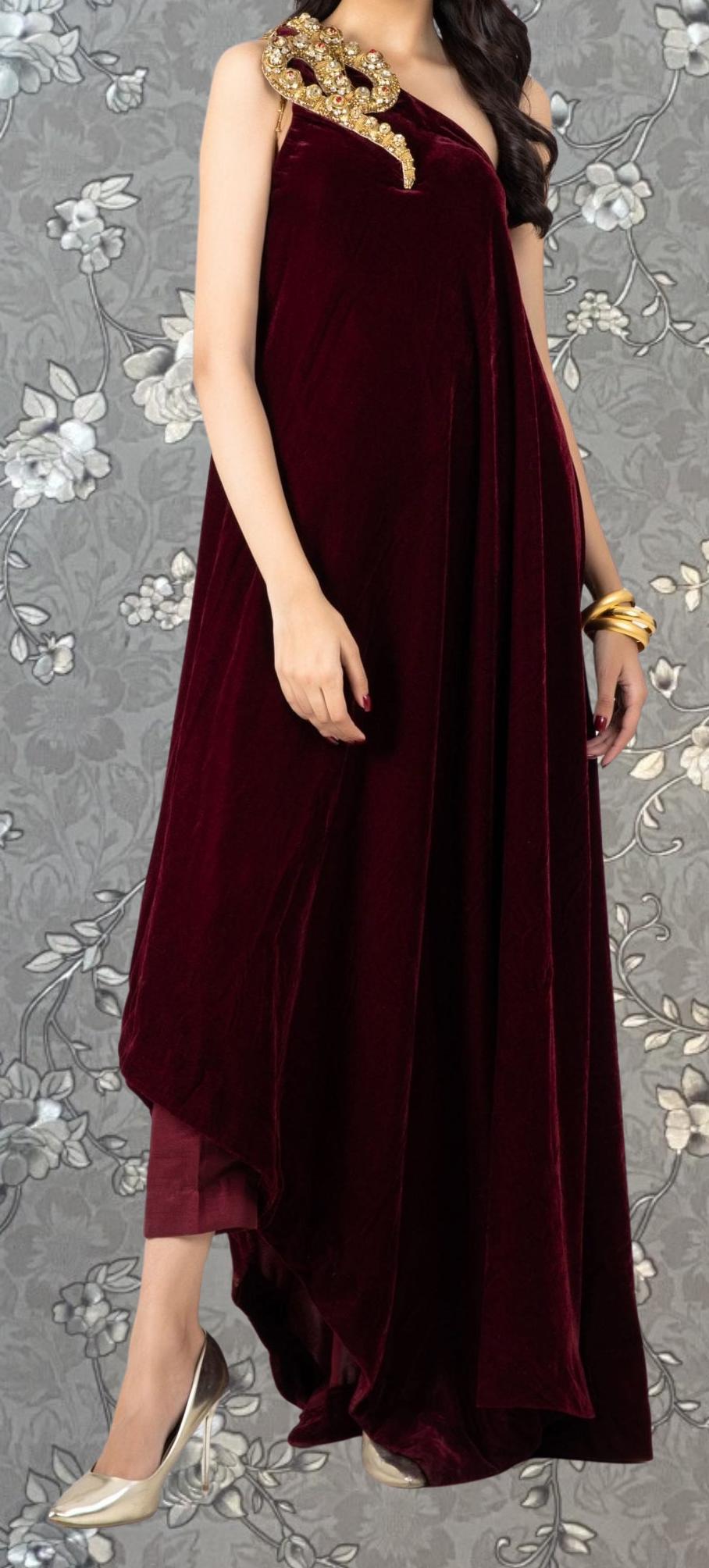 A woman wearing a burgundy velvet dress with a gold embellishment on the shoulder.