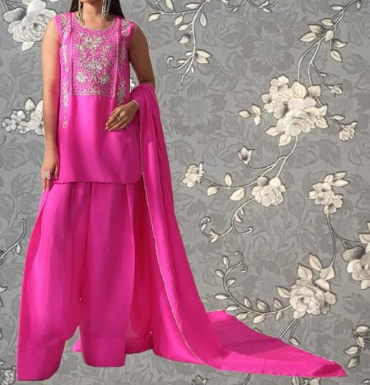 A woman wearing a pink dress with a long train and a matching pink shawl stands against a gray floral background.