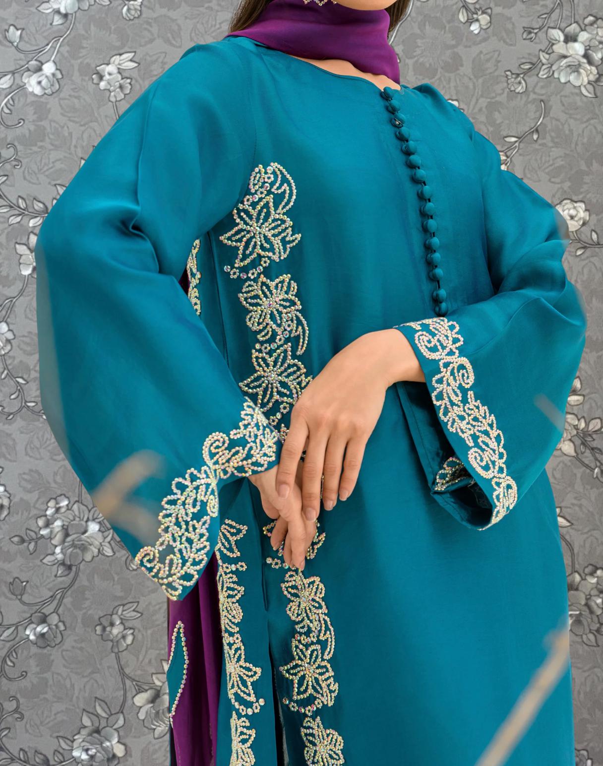 A person wearing a teal-colored dress with intricate embroidered patterns on the sleeves and hem.