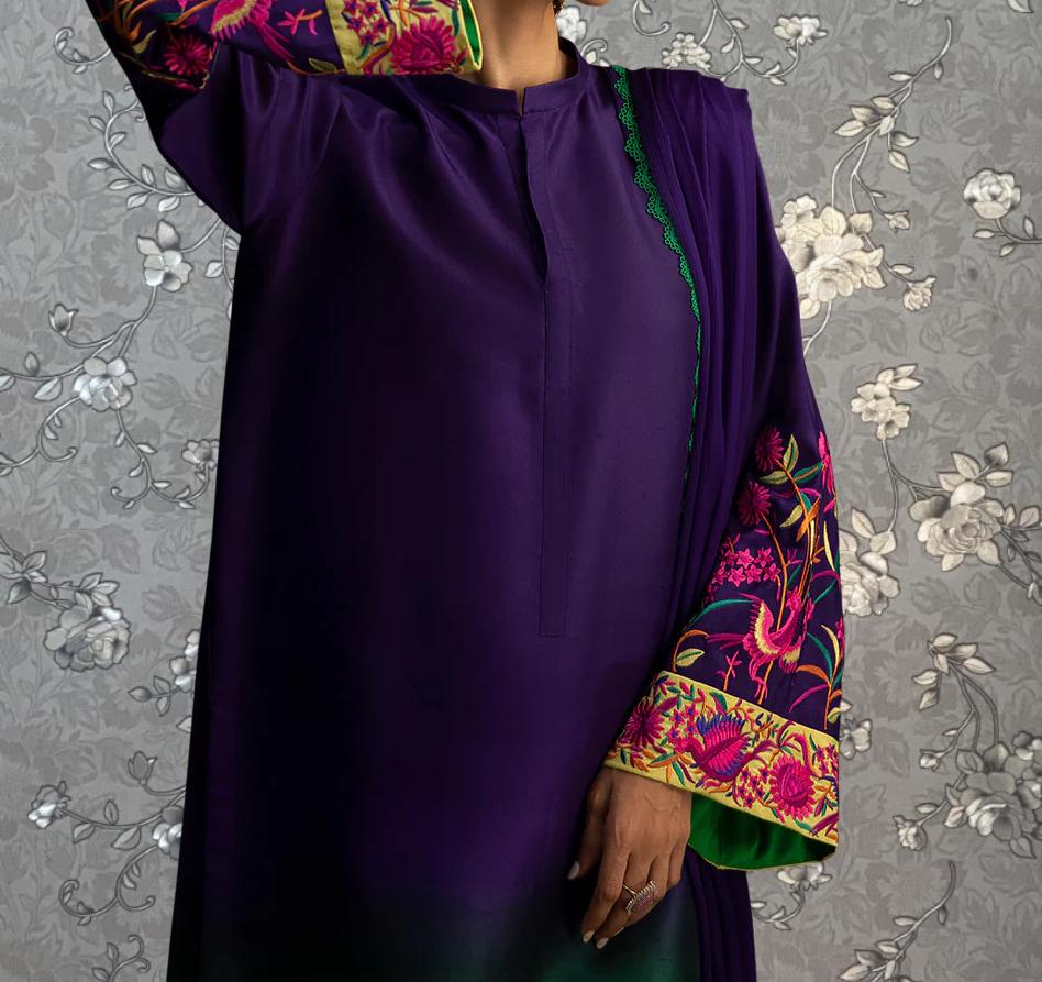 A person wearing a purple dress with intricate embroidered patterns on the sleeves and collar, posing against a gray floral background.
