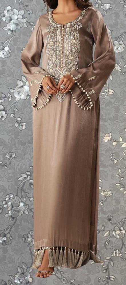 A woman wearing a long, beige dress with intricate embroidery and tassels at the bottom.