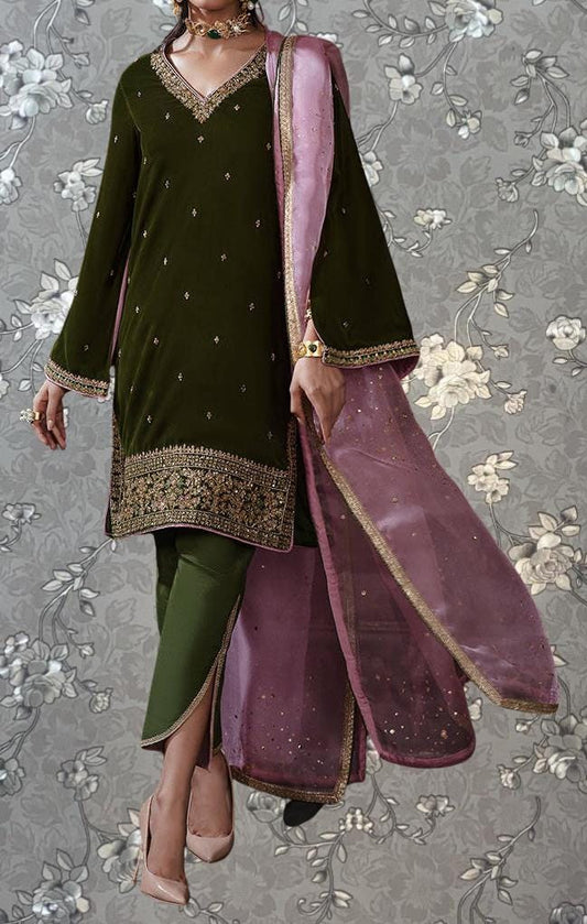 A woman wearing a green and pink embroidered dress with a matching shawl, standing against a gray floral background.