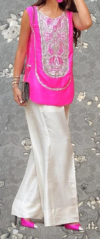 A woman wearing a pink sleeveless top with a floral pattern, white pants, and pink high heels stands against a gray floral background.