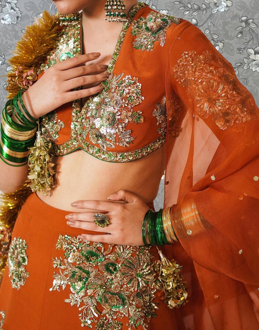 A woman wearing an ornate, colorful outfit with intricate embroidery and jewelry poses for a photograph.