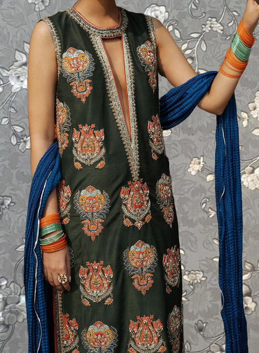 A person wearing a green and orange patterned dress with a blue scarf draped over their shoulders.