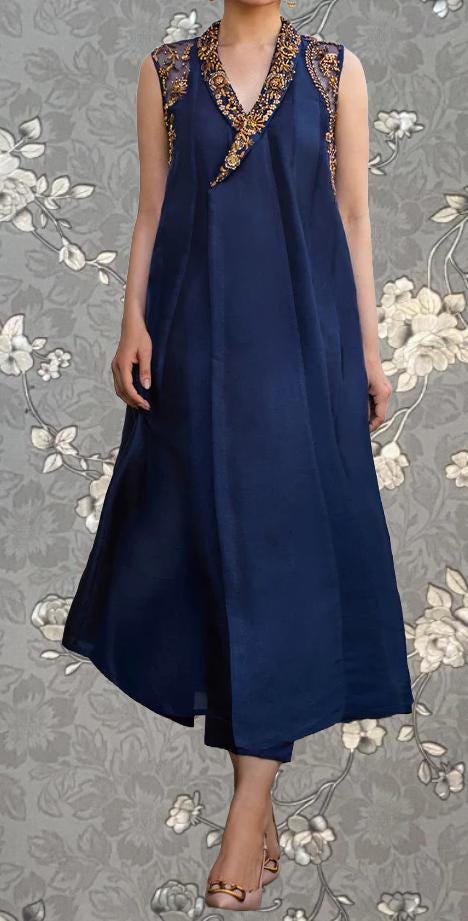 A woman wearing a navy blue dress with gold embellishments, standing against a gray floral background.