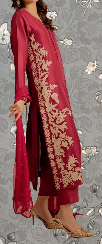 A woman wearing a red dress with gold embroidery stands against a gray floral background.