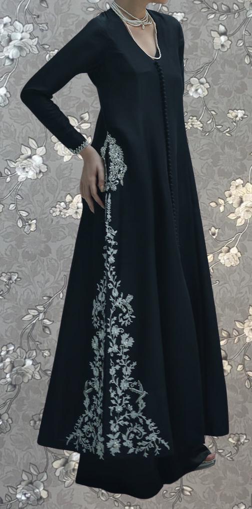 A woman wearing a long black dress with intricate white embroidery on the side.