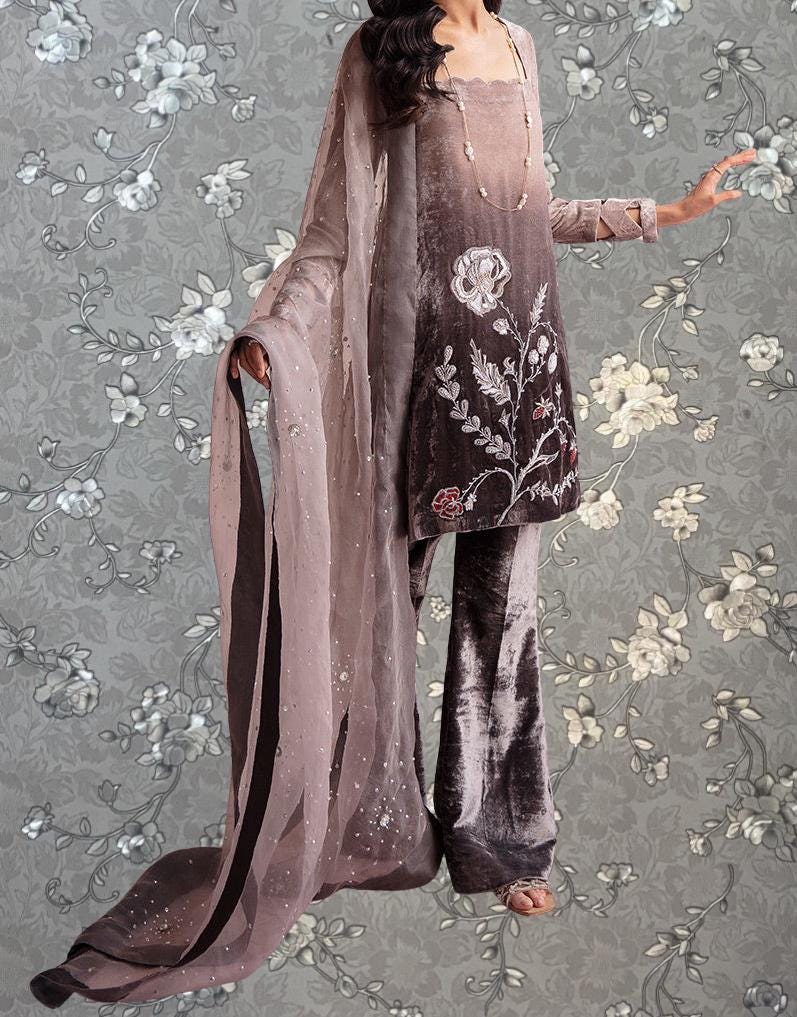 A woman wearing a long, flowing dress with a floral pattern and a matching shawl stands against a gray floral background.