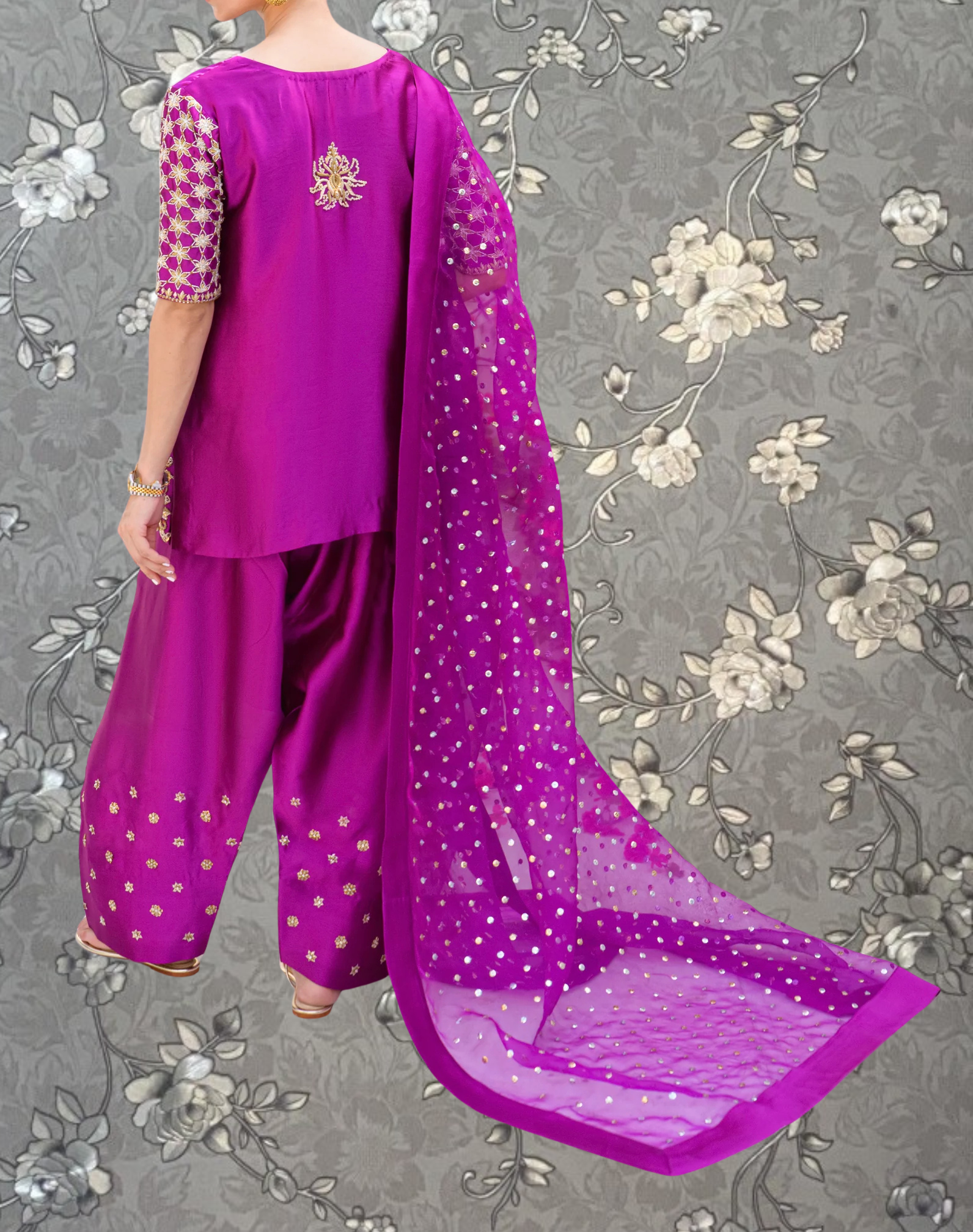 A person wearing a vibrant purple outfit with a long, flowing purple shawl and matching pants, standing against a gray floral background.