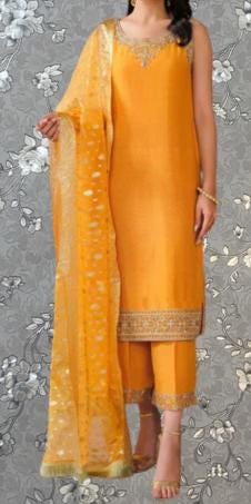 A woman wearing a bright yellow dress with a matching shawl and gold accents, standing against a gray floral background.