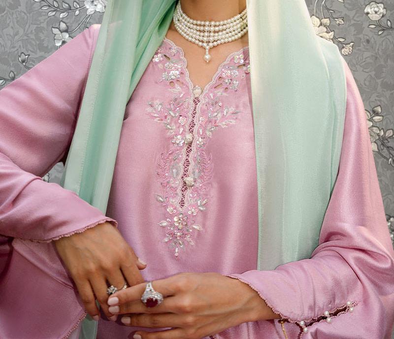 A woman wearing a pink dress with intricate embroidery and a green scarf, accessorized with jewelry.