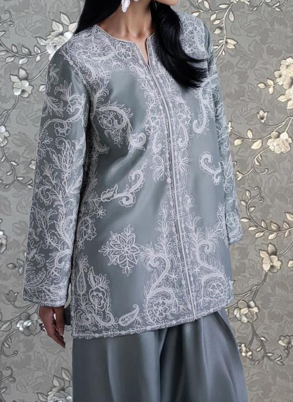 A woman wearing a gray and white patterned dress stands against a floral background.