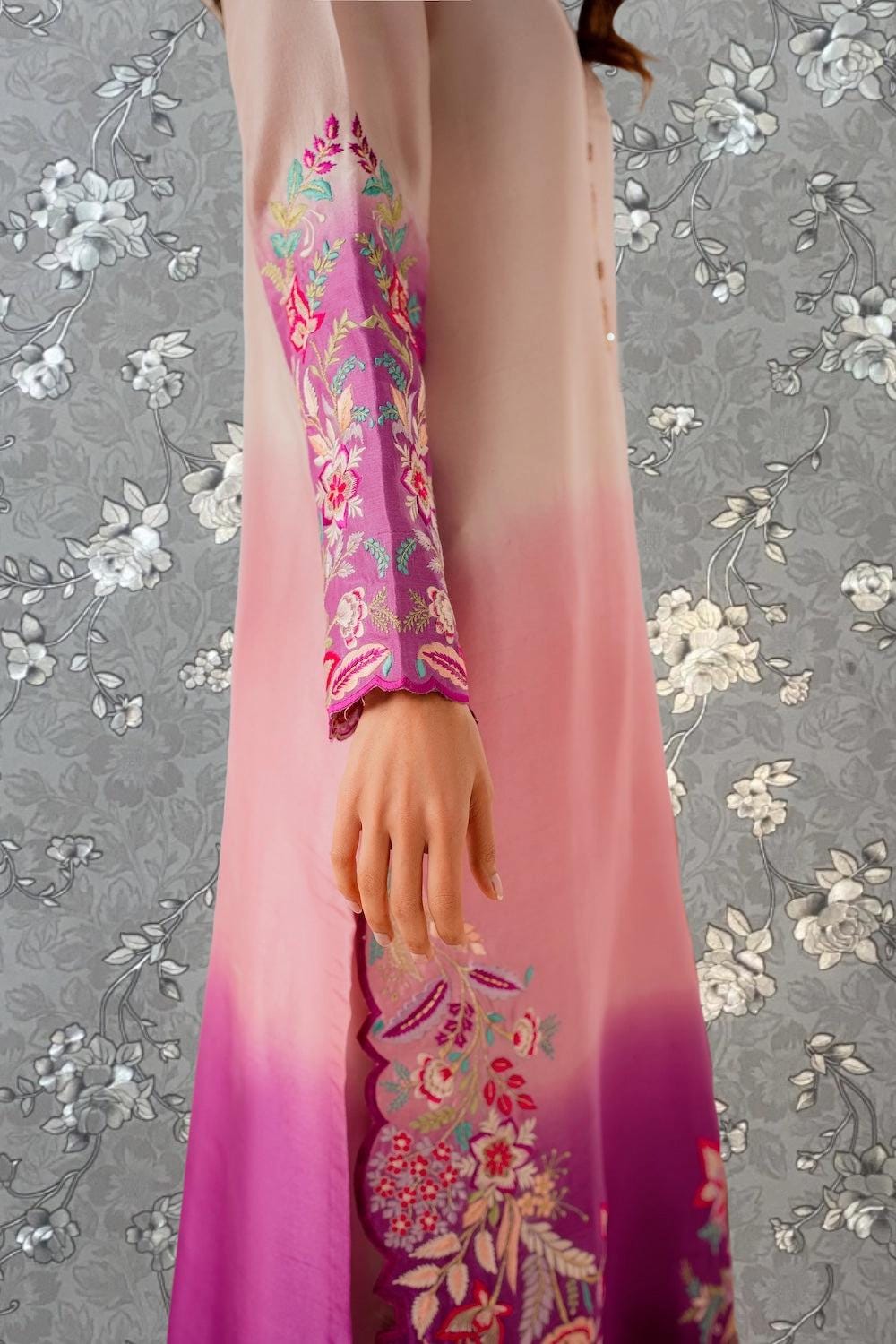 A woman wearing a long, flowing dress with a floral pattern in shades of pink and purple.