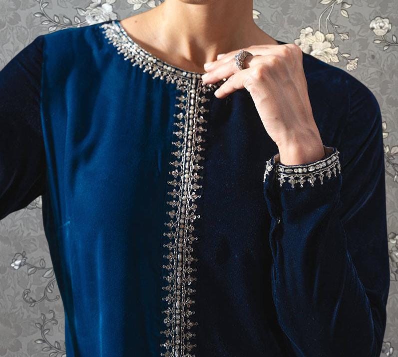 A close-up of a person wearing a blue velvet dress with a silver embroidered design on the collar and sleeves.