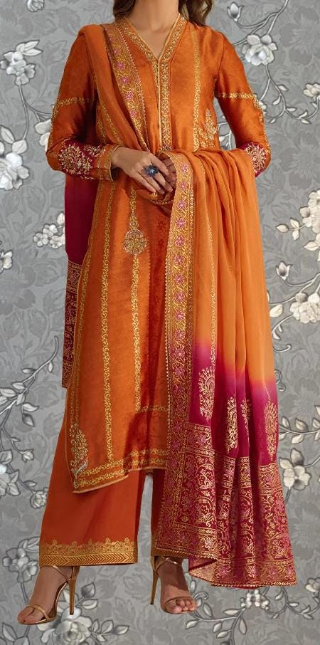A woman wearing an ornate orange and pink dress with intricate embroidery and patterns, standing against a gray floral background.