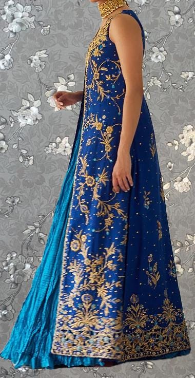 A woman wearing a long, blue dress with gold embroidery and a matching gold necklace.