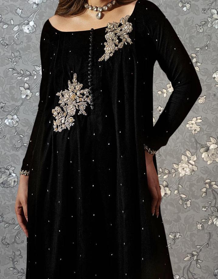A woman wearing a long black dress with intricate embroidered designs on the front.