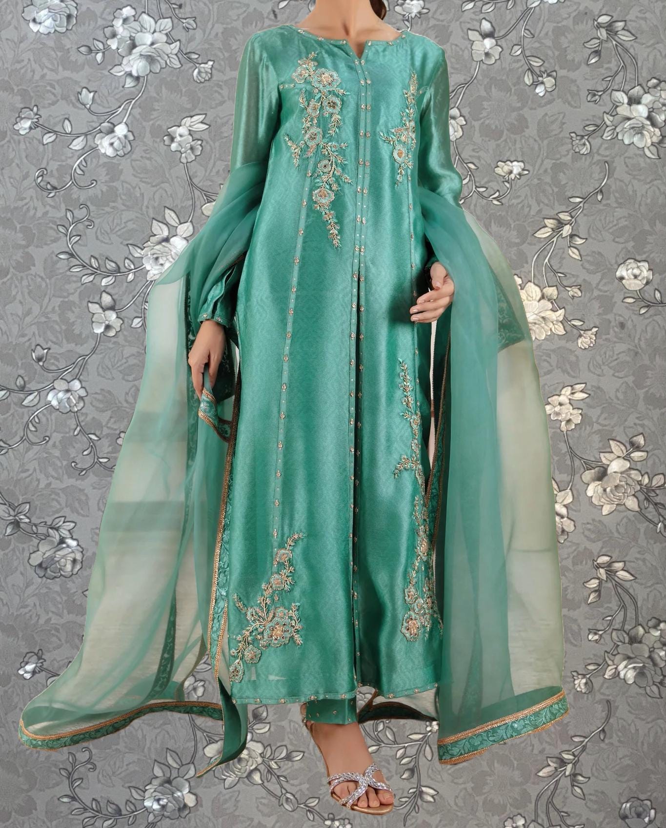 A woman wearing a long, green dress with intricate embroidery and a matching green shawl.