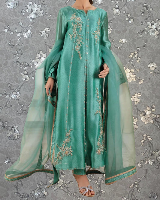 A woman wearing a long, green dress with intricate embroidery and a matching green shawl.