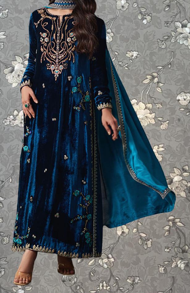 A woman wearing a long, blue velvet dress with intricate embroidery and floral patterns.